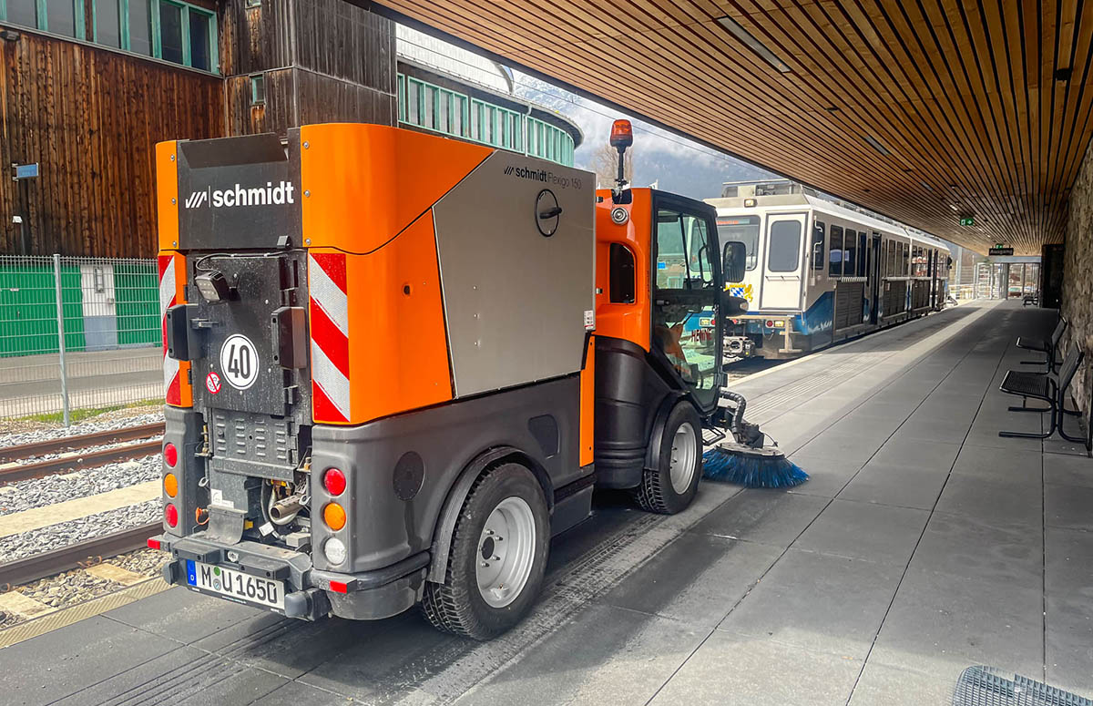 Die Kehrmaschine Flexigo 150 schräg von hinten aufgenommen auf dem Bahnsteig der Bayerischen Zugspitzbahn. Im Hintergrund sieht man die abfahrende Bahn.